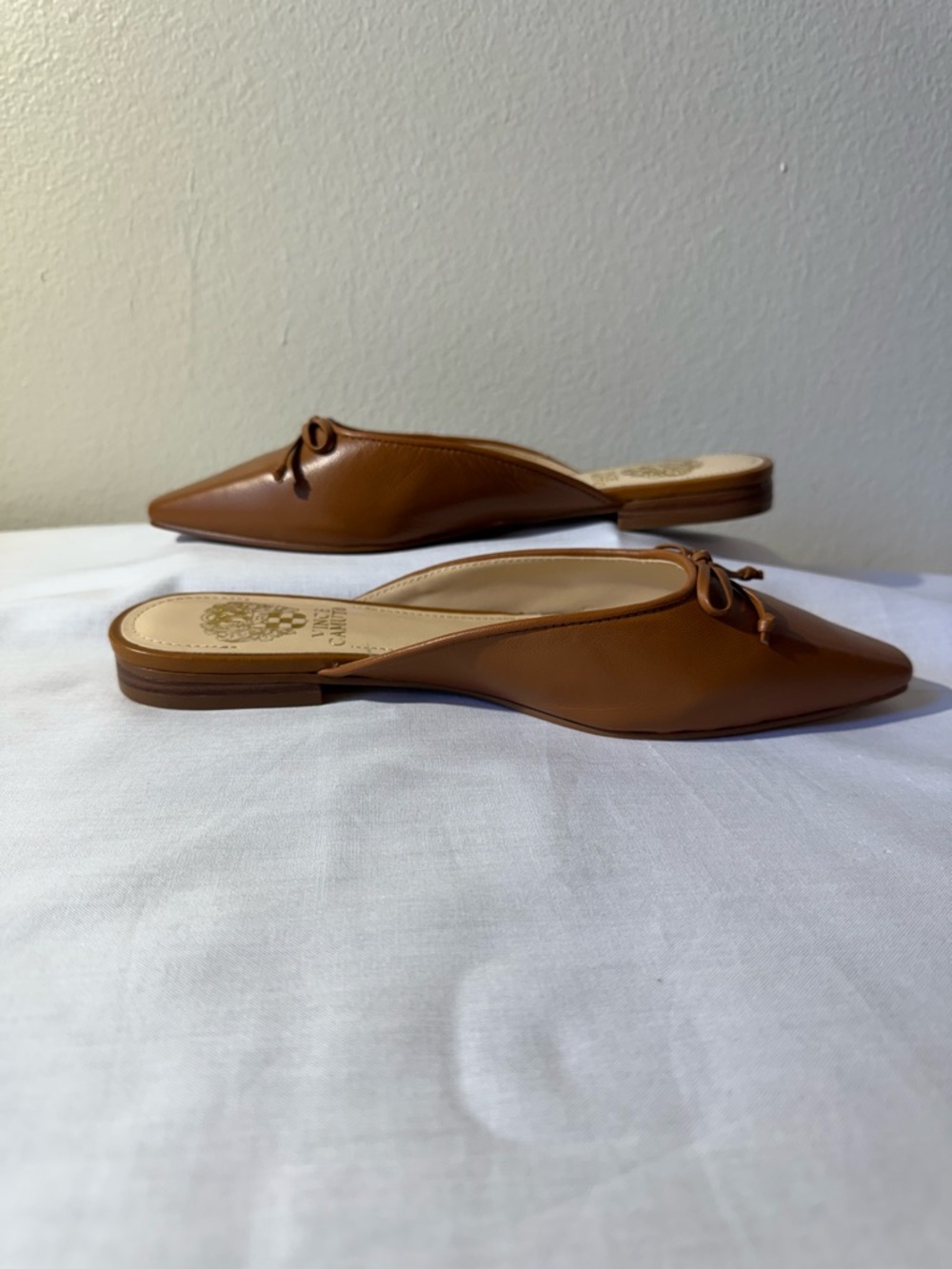 Vince Camuto brown leather flat mules featuring a pointed toe and a charming bow